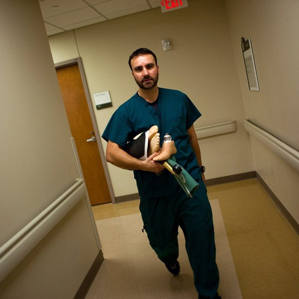 Zach walking down a hall carrying prosthetic limb parts and pieces