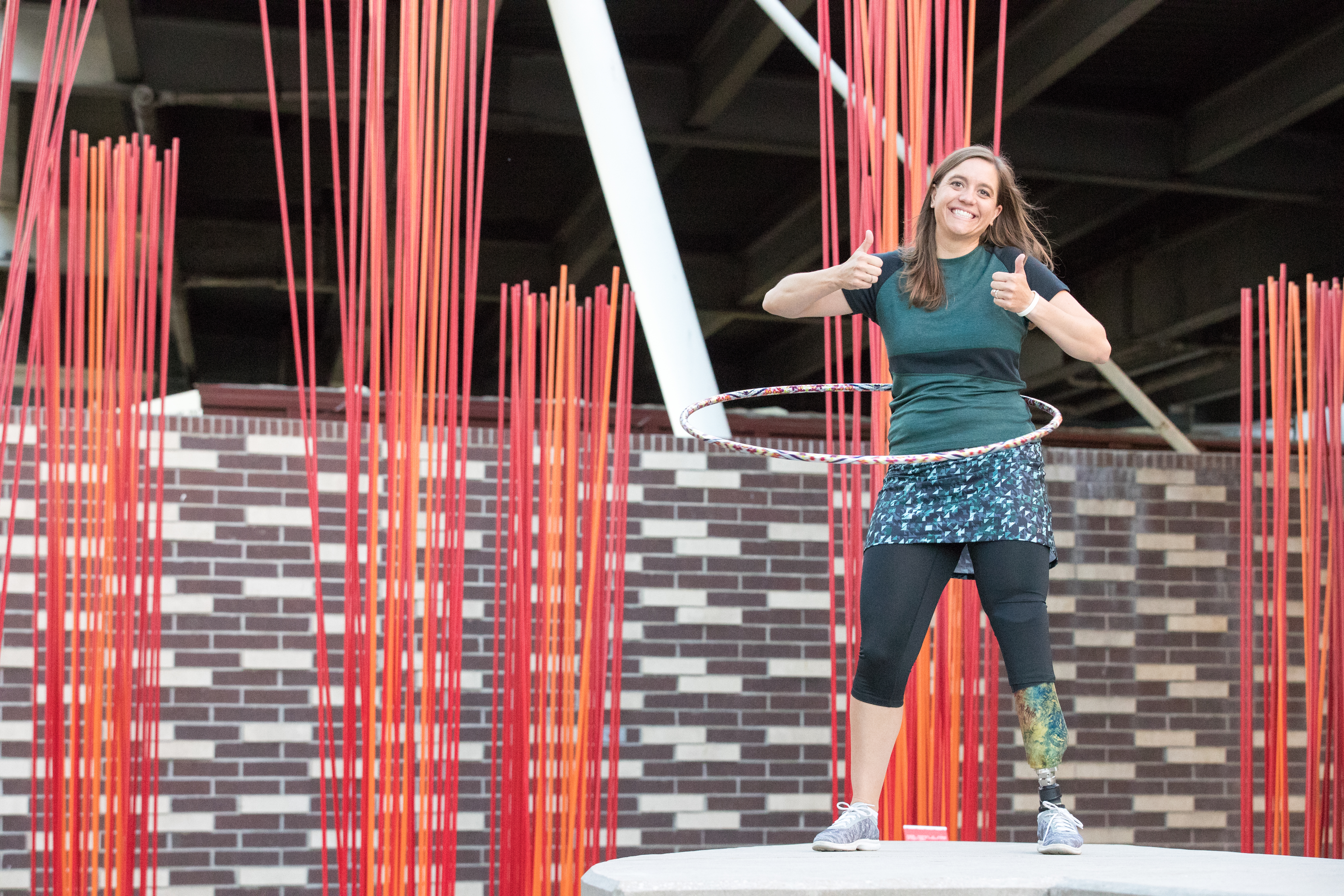 Emily hula hooping with the double thumbs up wearing Skirt Sports and with red and orange artwork in the background