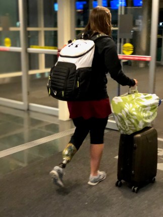 Emily walking at the airport with a backpack on her back and her rolling suitcase with her bag of legs attached on top