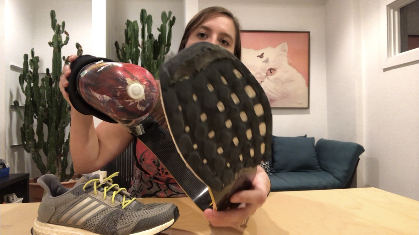 screen shot of Emily holding her running leg up to the camera to show the wear on the bottom of her running leg