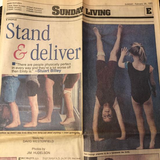 Front page of Section E of The Shreveport Times, Stand & Deliver, "There are people physically perfect in every way and they're a lot worse off than Emily is." - Stuart Billey, Story by David Westerfield, Photos by Jim Hudelson. Photo 1 of little kid legs, including my prosthesis, standing in a line. Photo 2: me doing a handstand and another blonde girl about to do one next to me.