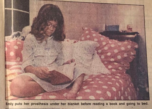 Photo of me reading in my bed with text below that reads, "Emily puts her prosthesis under the blanket before reading a book and going to bed."