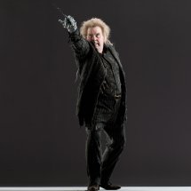 photo of wormtail with his silver hand holding a want out in front of him, wearing all black