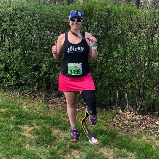 Me giving a thumb's up and holding my medal out to the side. I'm wearing my running, a pink running skirt, a black tank top that says 